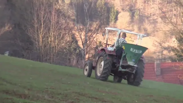 Traktor mit grünem Düngerstreuer kalkt eine Wiese am Hang